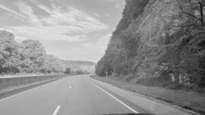 Black and white photo of an empty interstate curving past a rock cliff, evoking the quiet drive home after receiving hard news