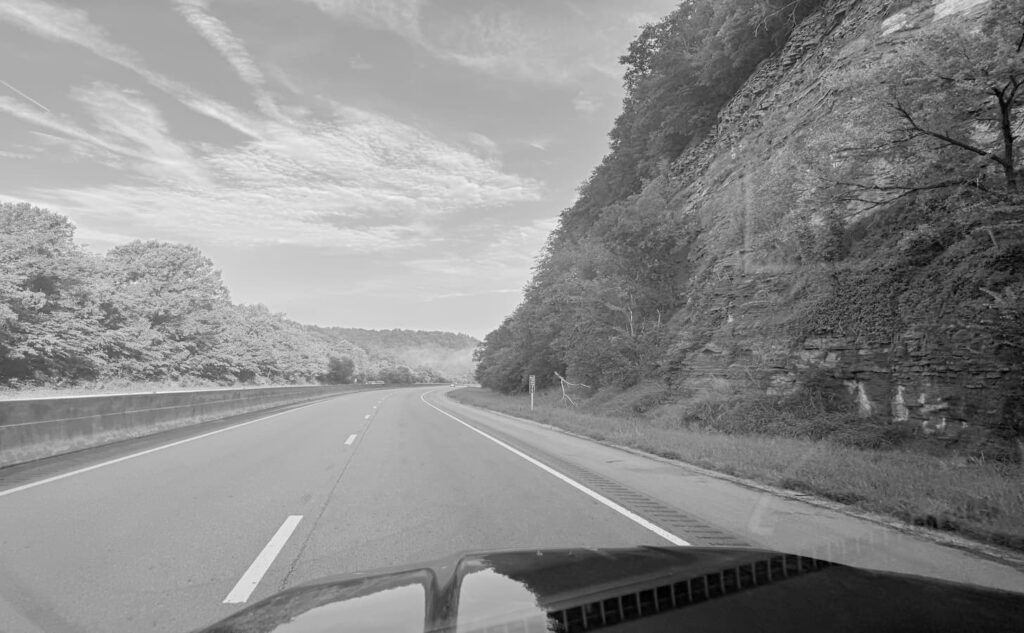 Black-and-white photo from a truck driver's seat on a Tennessee interstate cutting through a mountain rock face