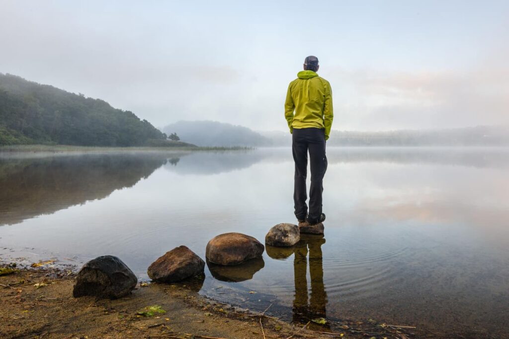 Man standing alone at a misty lakeshore at sunrise, reflecting the emotional denial before a cancer diagnosis