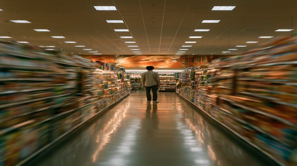 Blurred grocery store aisle with a lone man standing still, conveying the isolation of receiving a cancer diagnosis